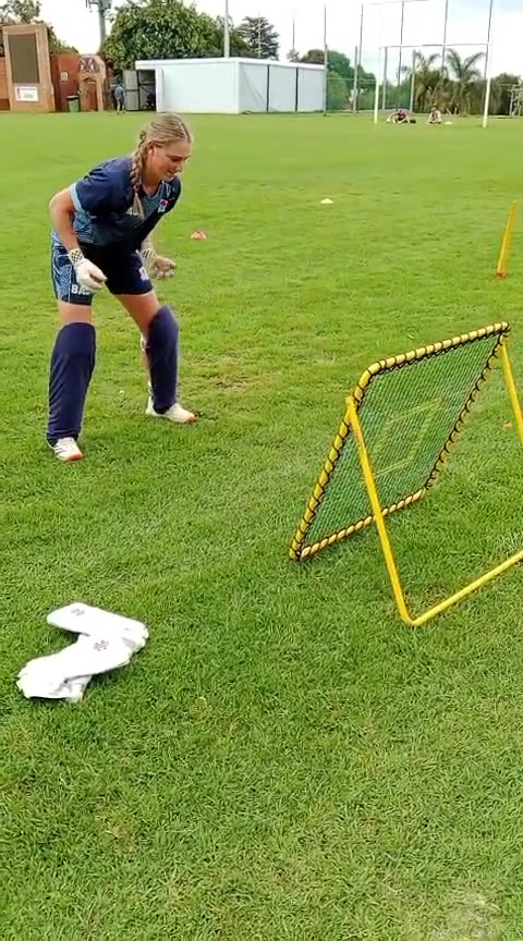 A wicketkeeper crouched beside the yellow Catch-It rebound net on a field