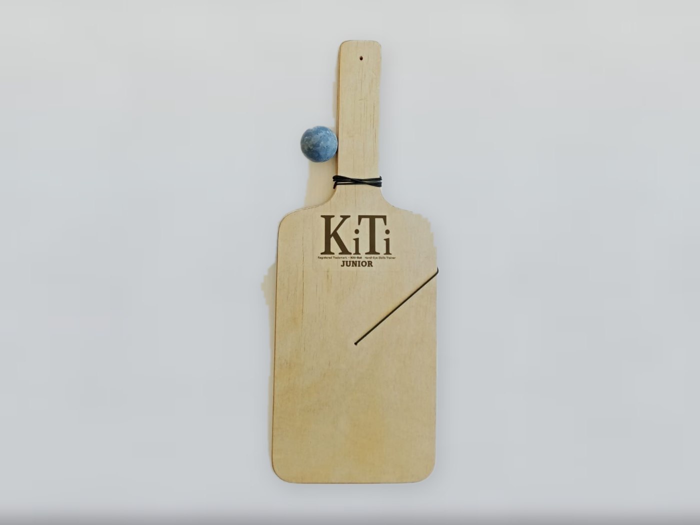 A KiTi Junior on its own: short wide plywood face with the KiTi Junior mark and the blue ball on its elastic string