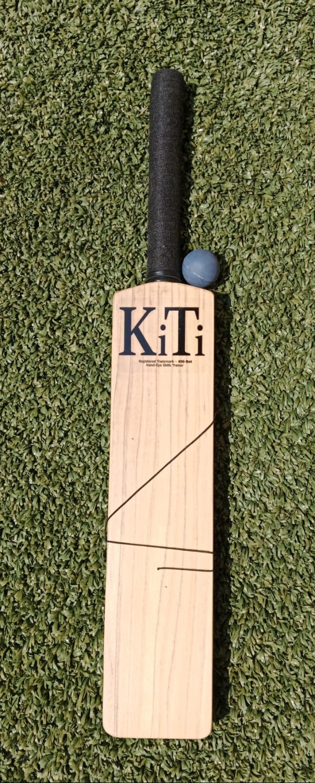 A KiTi-Bat lying on artificial grass with its blue ball